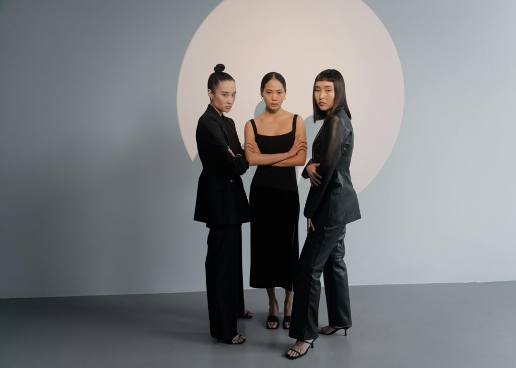 Stylish portrait of three women in black fashion against a minimalist backdrop.